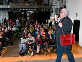 Dritter Bürgermeister Metzner preist vor vollem Haus im Großen Saal des Alten E-Werks eine rote Tasche zum Verkauf an