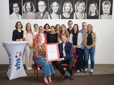 Foto: Stadtarchiv Bamberg, Nadine Gumpert vhs-Leitung Dr. Anna Scherbaum und Oberbürgermeister Sebastian M. Niedermaier halten die Urkunde des 3-Sterne-Assessments in den Händen. Dahinter das vhs-Team